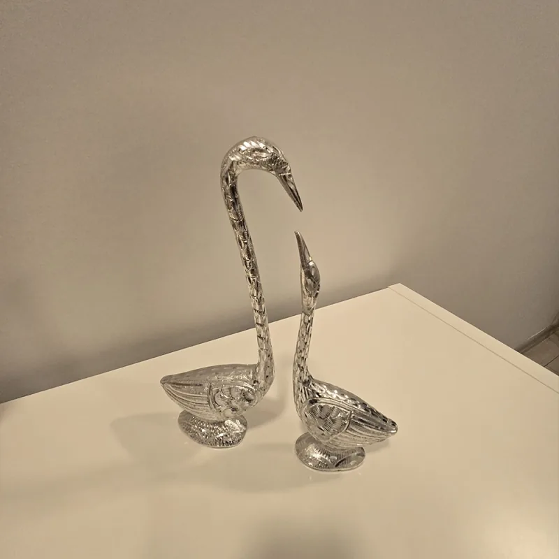 Zwei silberfarbene Schwanfiguren auf einem Tisch